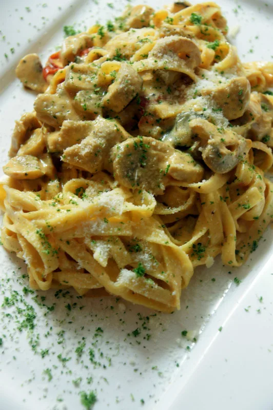 Romige tagliatelle met champignons, geraspte parmezaan en peterselie op een wit bord